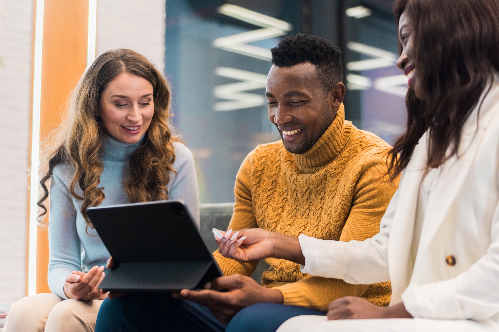 Multiracial group of people in an office discussing business using a tablet while sitting on a sofa